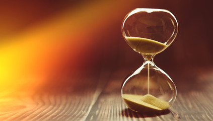 The sunbeam penetrates the hourglass, symbolizing the beginning of time or the final time. Clock on a wooden background.