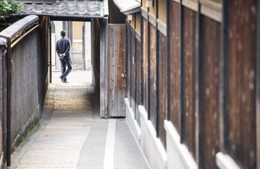 Fototapeta na wymiar Unidentified man in dark suit stands in doorway to alley between traditional Japanese wooden buildings