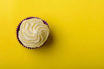 Cupcake in purple wrap on yellow background. Minimalism. Top view with copy space.