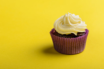 Cupcake in purple wrap on yellow background. Minimal. Copy space.