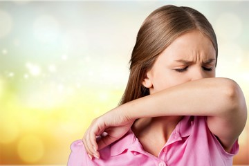 Young woman scratching her nose with elbow on dark gray background