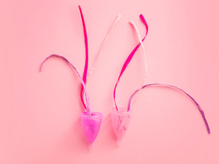 Obraz na płótnie Canvas Close up of menstrual cup and ribbons over pink background. Eco-friendly concept for women's health. Innovation product in gynecology that replaced traditional approaches.