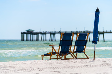 Okaloosa fishing pier in Fort Walton Beach, Florida in Panhandle, Gulf of Mexico on summer sunny day, two empty beach recliner lounge chairs umbrella