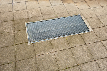 Ein Lichtschacht mit einem Gitterrost in einem Weg aus Platten aus Beton