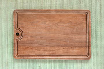 Brown wooden cutting board on background of a rough green mat made of natural plant fibers. Cooking copy space. Top view