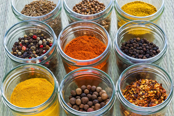 Set od nine different spices and herb seasonings in a glass jars on a rough green mat. Natural food spices and seasonings. Tasty eating.