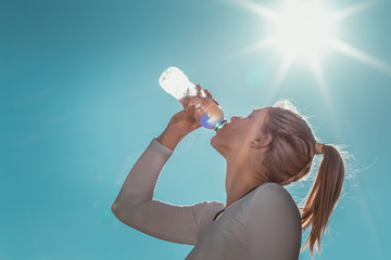 Blonde, sporty woman drinking water after her training in the morning.