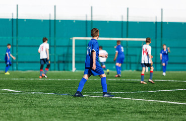 Boys at blue white sportswear run, dribble, attack on football field. Young soccer players with ball on green grass. Training, football, active lifestyle for kids