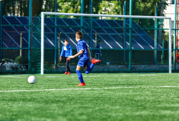 Boys at blue white sportswear run, dribble, attack on football field. Young soccer players with ball on green grass. Training, football, active lifestyle for kids