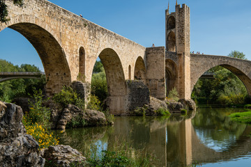 Fototapeta na wymiar Girona, Spain - Sept 24 2018: View from under the romanesque bridge across Fluvia river with arches and defence towers in Besalu, Girona, Spain.