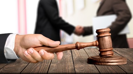 Wooden judge hammer, handshake of business people on background