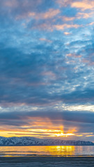 Vertical frame Lake and snow capped mountain underneath a sky filled with clouds at sunset
