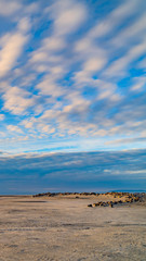 Vertical frame Boundless blue sky with gray and white clouds over a vast sandy shore