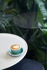 coffee latte in green cup on white table on atmosphere nature surrounded background.
