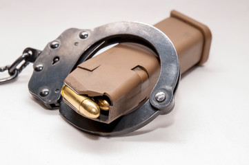 A brown 9mm pistol magazine loaded with full metal jacket bullets inside of a black metal handcuff on a white background