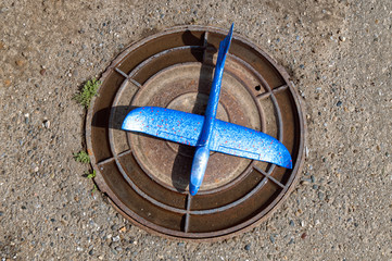 Blue toy airplane on steel round manhole cover.