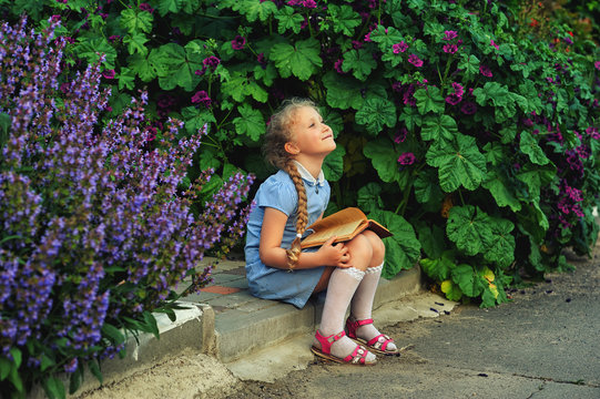 Beautiful little girl reading a book sitting on the street .The concept of additional education
