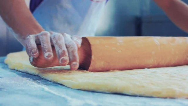 	Man rolling dough on the table with a wooden rolling pin. Close up