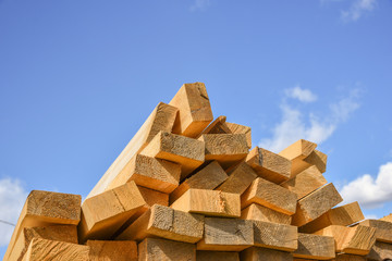 Stacked lumber on blue sky.Folded wood.Closeup wooden boards.The surface of the end of the board.Lots of planks stacked on top of each other in the warehouse.Lumber for use in construction.