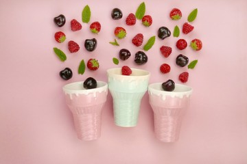 Summer berries. Berry ice cream. Strawberries, raspberries, cherries with leaves and ice cream cups on a light pink background. Summer sweets concept.