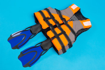 orange life jacket and pair of blue flippers, on blue background, concept of safe diving and...