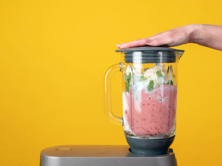Blender on a yellow background. Strawberries, milk, mint, ice cream. Preparation of milky fruit drinks, smoothies, shake, cocktail.