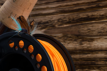 reel with orange fishing line and feather bait lie on a wooden background