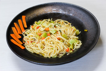 spaghetti dish with vegetables, black dish, white background, selective focus