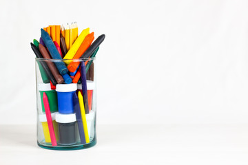 Many colourful crayon and School Supplies in glass bowl,  isolated on a white surface.