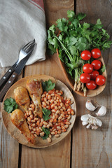 fried chicken legs with beans and tomatoes on a wooden plate