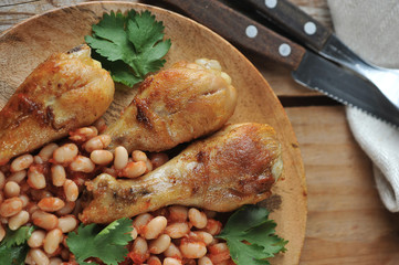 fried chicken legs with beans and tomatoes on a wooden plate
