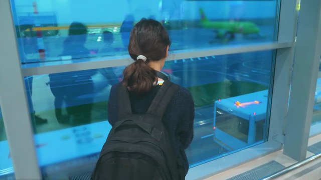 daughter with a backpack airplane flights airport concept. girl teenager with a smartphone looks out the window at the airport area airplanes and bus at a distance. lifestyle teen girl looks at the