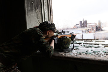 Girl sniper looks through the scope. Girl warrior directs his rifle through the broken window of an abandoned building. Military service for girls.