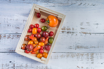 Colorful tomatoes in a wooden box on white wooden table. Top view, copy space, soft focus..