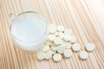 Mug of milk and round milk pellet pile on space of pine wood