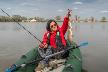 Kayak fishing. Fisher girl holding pike fish trophy on inflatable boat with fishing tackle at lake.