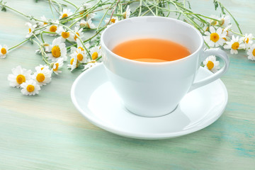 A cup of chamomile tea on a teal blue background with a bouquet of flowers and a place for text