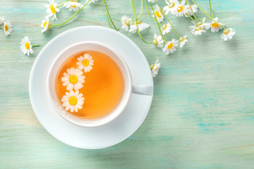 A cup of chamomile tea, shot from the top on a teal blue background with flowers and copy space