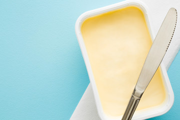 Opened plastic pack of light yellow margarine and knife. Closeup. Empty place for text or logo on pastel blue desk. - obrazy, fototapety, plakaty