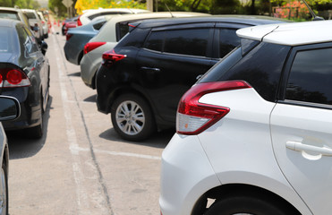 Closeup of rear side of white car with  other cars parking in outdoor parking lot beside the street with natural background in bright sunny day. 