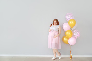 Fototapeta na wymiar Beautiful pregnant woman with baby booties and balloons near light wall