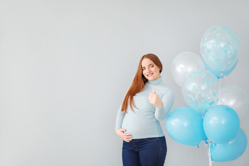 Beautiful pregnant woman with balloons showing thumb-up on light background