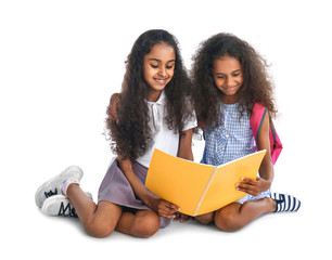 Cute African-American schoolgirls with book on white background
