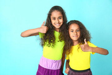 Fototapeta na wymiar Cute African-American girls showing thumb-up on color background