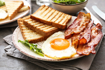 Plate with tasty grilled bread, fried egg and bacon on table
