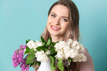 Beautiful young woman with bouquet of lilac flowers on color background