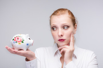 Fototapeta na wymiar young red haired woman with her piggy bank is thinking