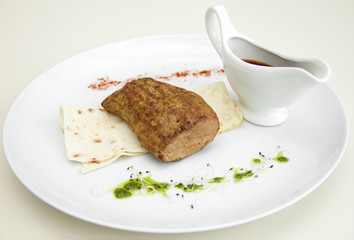 grilled meat on a white plate, sauceboat with sauce, restaurant serving