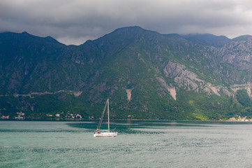 Lonely yacht sailing in the bay in the background mountains.