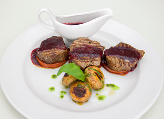 grilled meat medallions on a vegetable plate, sauce in sauceboat, restaurant serve